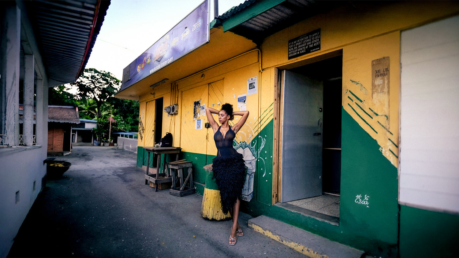 Woman in a black dress standing in front of a yellow building with green accents.
